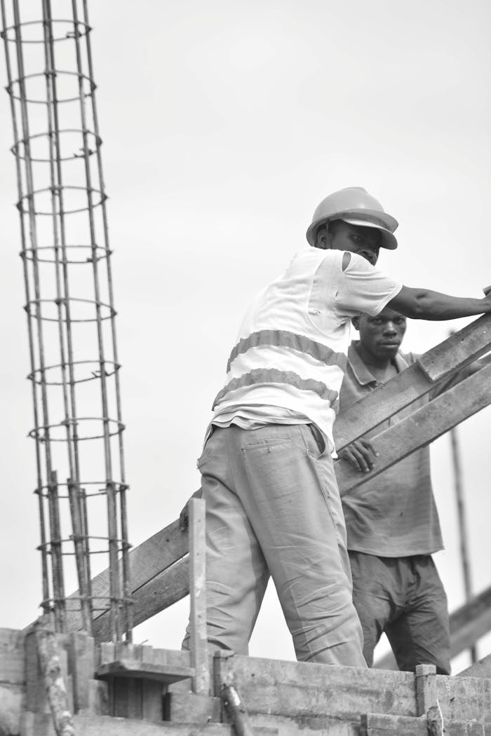 Services Black and white image of two construction workers wearing safety gear and helmets at a building site.