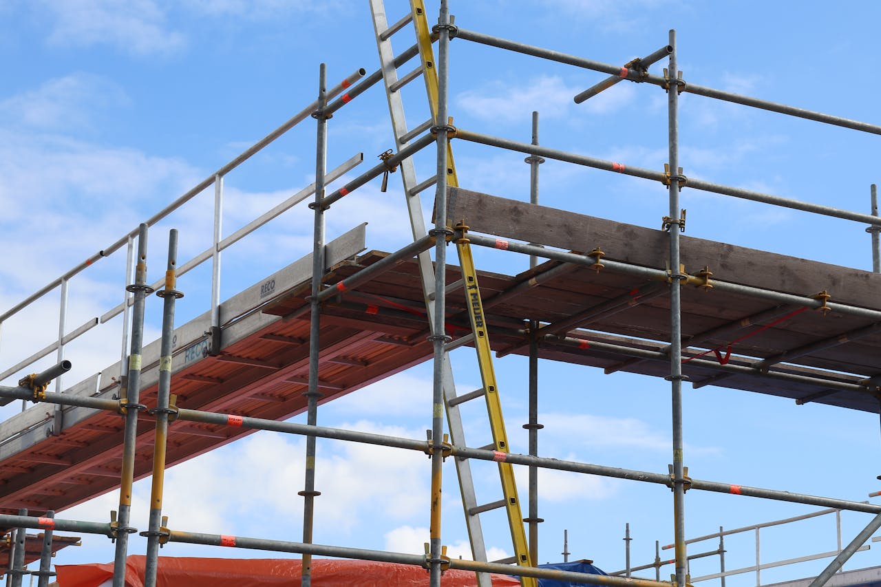 Services Detailed view of a construction site scaffolding structure and ladder against a bright blue sky.