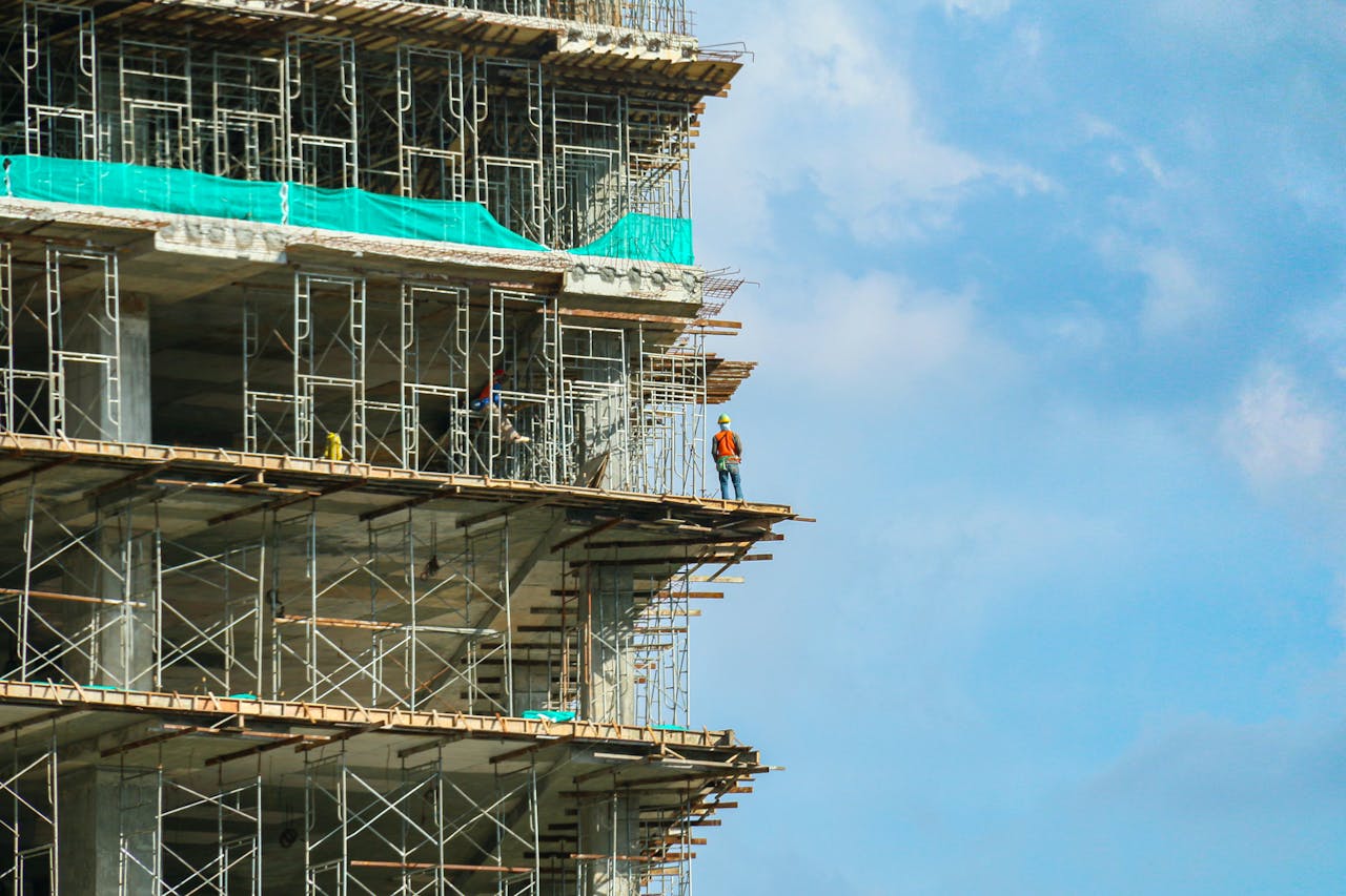 About A construction worker stands on a scaffolding at a high-rise building under a blue sky.