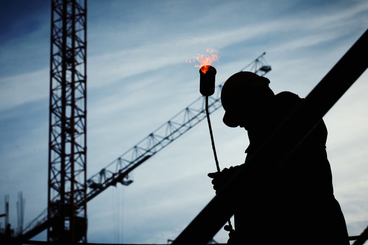 Services Silhouette of a construction worker using a blowtorch at a building site against a crane-filled skyline.